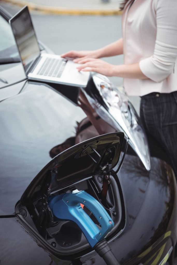 Woman using a laptop beside a charging electric car